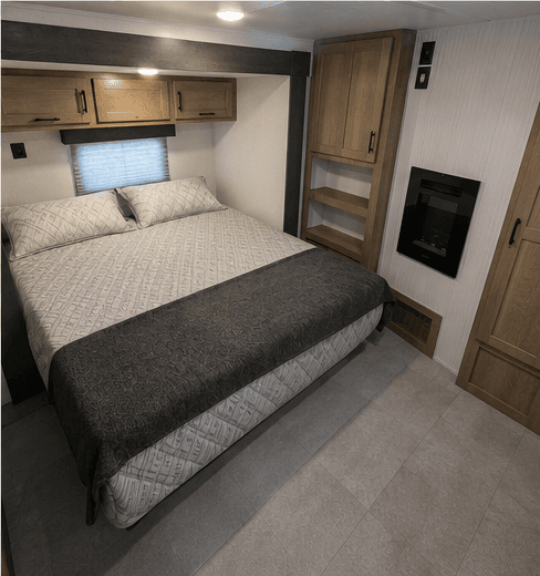 Main bedroom with a made bed, overhead cabinets, shelving, and a fireplace