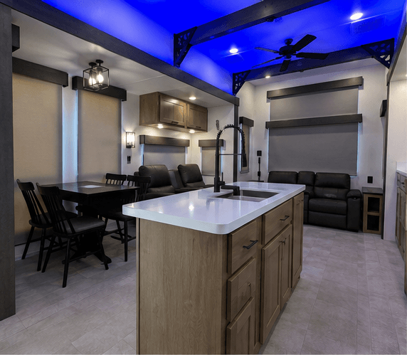 Kitchen island with quartz top looking across to the dining table and recliners, accent lighting along the ceiling beams