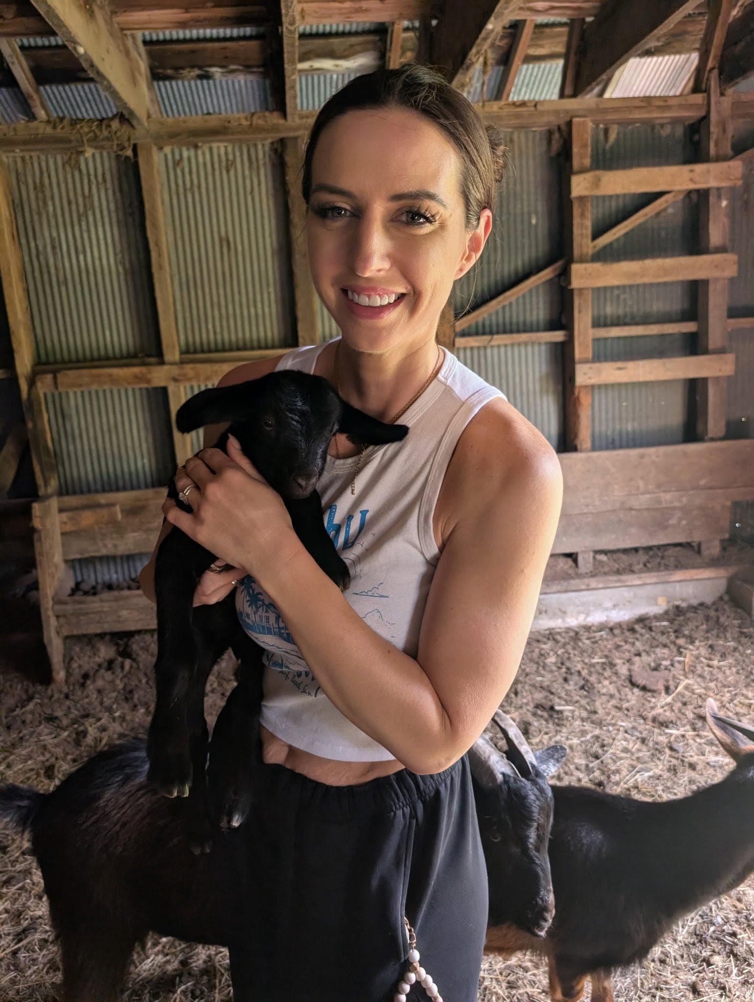 Mandy in the barn holding one of the property's black goat kids, with the herd around her