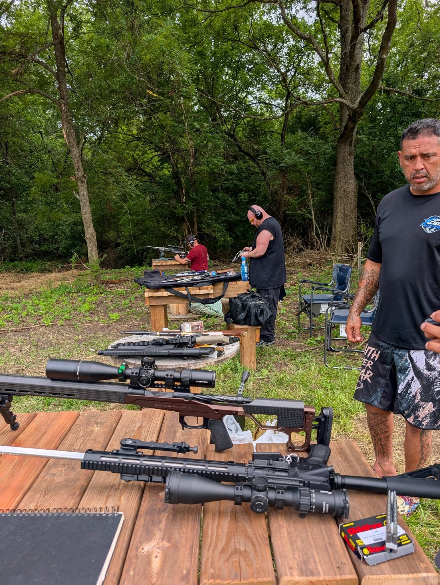 Members at the shooting benches, rifles staged in the foreground